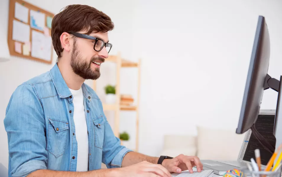 Java-Programmierer mit Bart, blauem Hemd und weißem T-Shirt, der an einem Computer arbeitet
