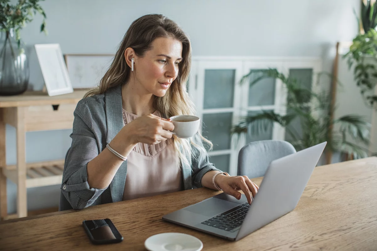 Female devops engineer holding a cup of coffee and working on a laptop