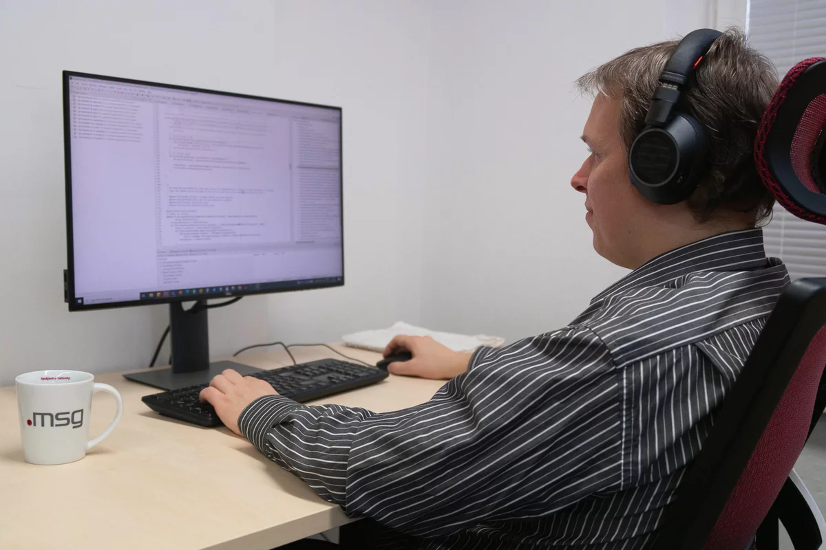 Java programátor pozerá do kódu do monitora na stole s hrnčekom msg life 