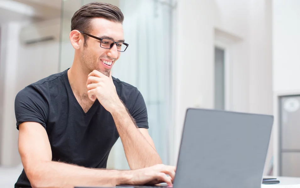 Mladý muž programátor sa usmieva pri práci na laptope