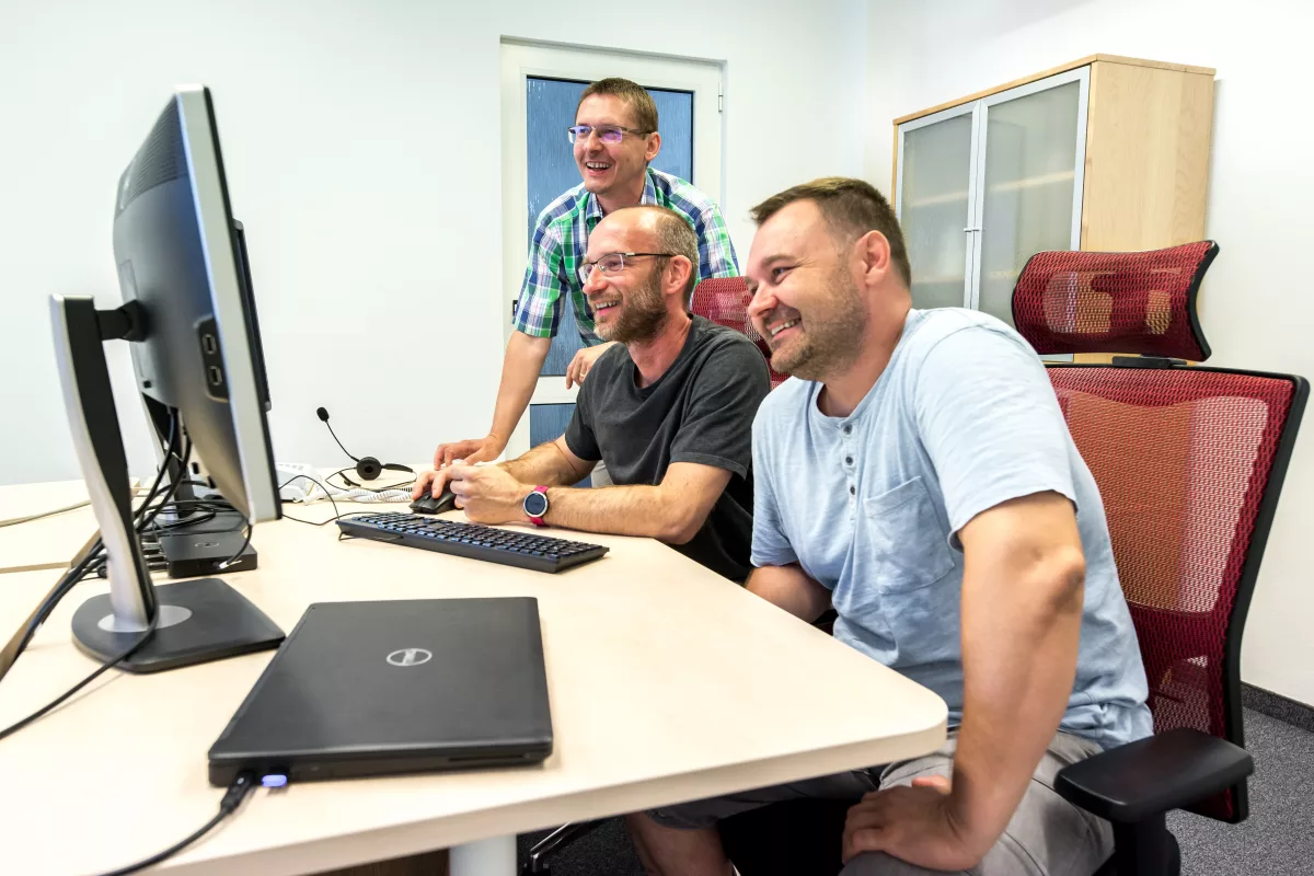 traja programátori kolegovia v msg life s dobrou náladou za stolom s monitormi